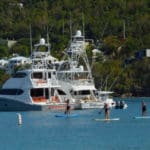 locals paddleboard in shadow of yachts