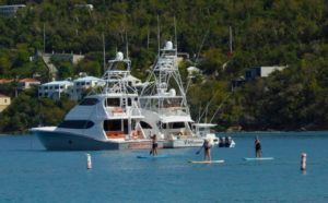Locals paddleboard past a line of visiting yachts. (Source photo by S. Pennington)