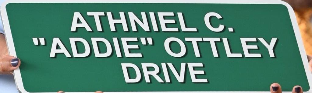 A family member holds a miniature of the sign naming a section of road in Sub Base, St. Thomas, after the late Athniel C. "Addie" Ottley. (V.I. Legislature photo by Barry Leerdam)