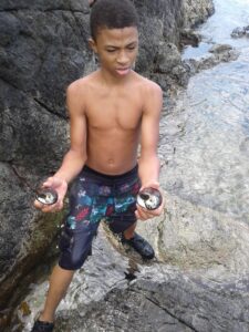 Mahsai Meyes, who hiked with me , a young Crucian boy at Annaly Bay rough coastline picking whelks.. From the shore of Annaly Cove, Annaly Bay, Annaly Notch, Wells Bay, Wills Bay, and Sweet Bottom Bay, you will see at times fishermen tending their fish pots. (Photo by Olasee Davis)