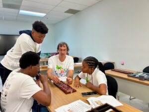 Dr. Adam Parr plays a game of Mancala with Umojah-I Lloyd, Aaliyah Paul and (standing) Gianni Ayala. (Source photo by Nyomi Gumbs)