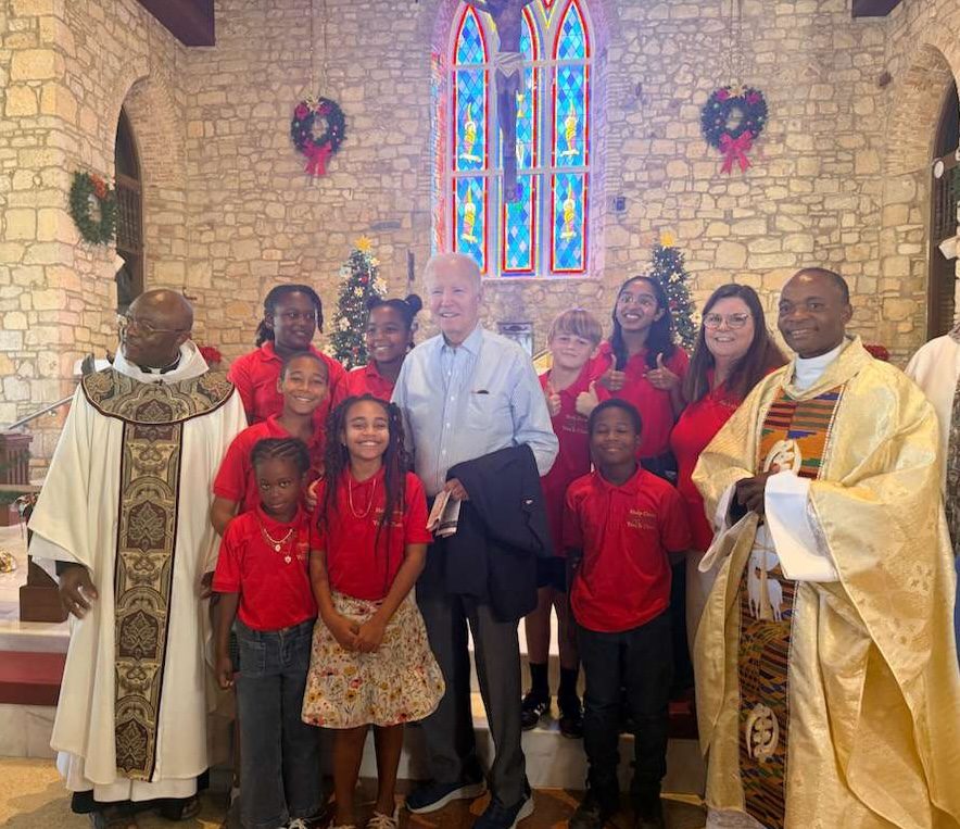 Former President Joe Biden pauses for a photo with members of the children's choir and the Rev. Louis Kemayou on Sunday at Holy Cross Catholic Church on St. Croix. (Source photo by Shanell Spencer)